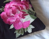 Black cushion with large bright pink embroidered flower.