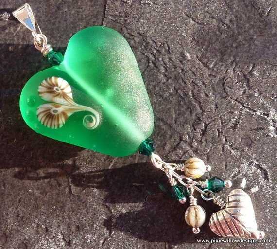 A pretty heart bead measuring 25mm from the top of the lobes to the bottom. Made on a base of a beautiful transparent teal white with a stylised swirled murrini heart on both sides