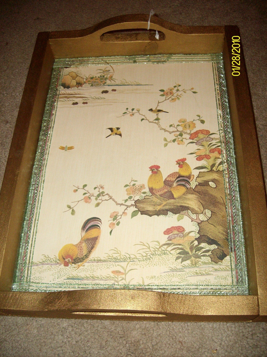 This is a beautiful wooden tray that has been painted gold and then has an oriental printed wallpaper on the bottom with roosters on it.